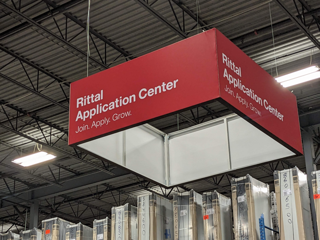 A red square hanging sign with Rittal Application Center written on it.